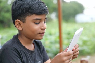 Indian little boy using digital tablet while attending the online classes at home with nature outside environment	
