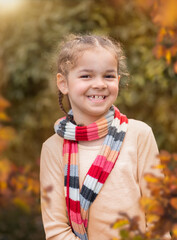 Smiling cheerful girl wearing striped scarf outdoors in autumn leaves  - 396465340