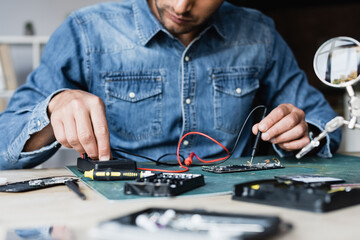 Cropped view of repairman using multimeter while holding sensor on disassembled part of mobile phone on blurred foreground