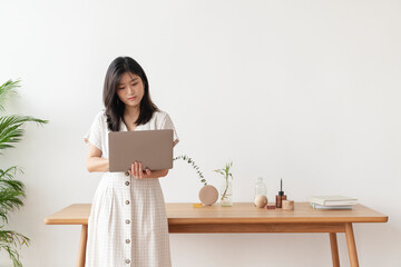 Asian woman standing by the wooden table using a laptop