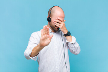 bald man covering face with hand and putting other hand up front to stop camera, refusing photos or...