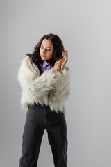  young woman in stylish white faux fur jacket posing on grey background