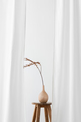 Dry Forsythia branch in a wooden vase on a stool by a white curtain