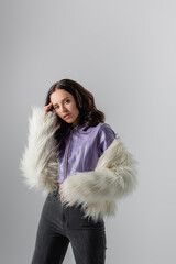  young woman in stylish white faux fur jacket posing on grey background