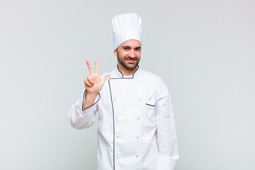 bald man smiling and looking friendly, showing number three or third with hand forward, counting...
