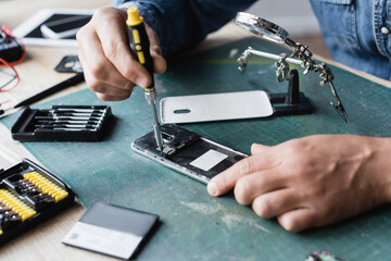 Cropped view of repairman with screwdriver fixing disassembled mobile phone at workplace on blurred background