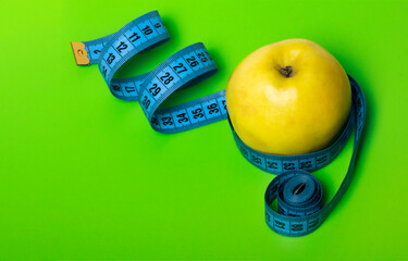 yellow Apple with blue measuring tape on green background diet and sports concept with a copy of the space
