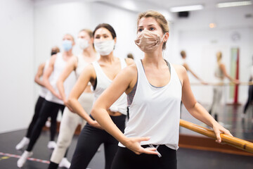 Naklejka na ściany i meble Group of men and women in protective masks practicing at the ballet barre