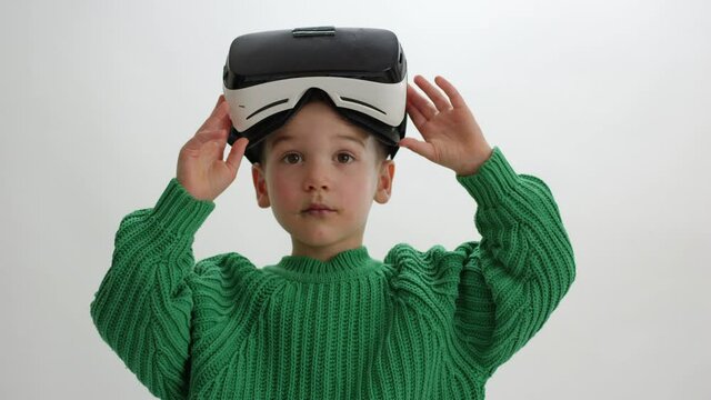 Young boy playing in virtual reality lifts up VR goggles from eyes - wide shot