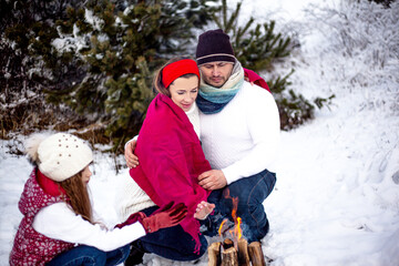 Happy family warm up near bonfire in the frosty snow forest while walking in the frash air