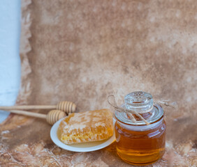 Fototapeta premium glass jar full of honey, plate with honeycomb on light brown background