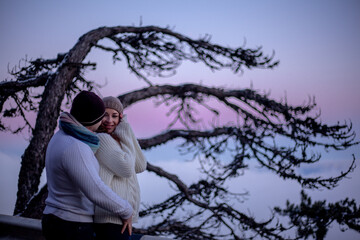 happy couple in sweaters hugging outdoor in snow day. The people above the clouds in the evening look at the blanket from the cloud
