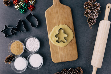 Christmas Ginger Bread Man Cookie Cutter In Raw Cookie Dough With Pine Cones, Holiday Ribbons, And Ingredients on Dark Slate Texture