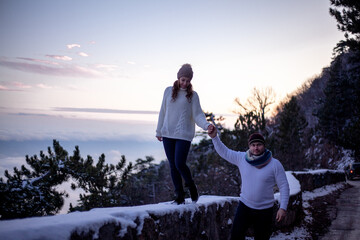 happy couple in sweaters hugging outdoor in snow day. The people above the clouds in the evening look at the blanket from the cloud