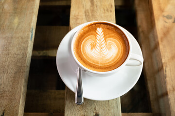 Cup of cappuccino with leaves shape latte art on a pallet coffee table with glass top. Cappuccino coffee in white cup and saucer.