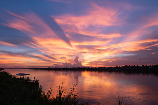 Sunset and light beam with colorful clouds over the Mekong riverbank. Orange and purple twilight sky reflection on water background.