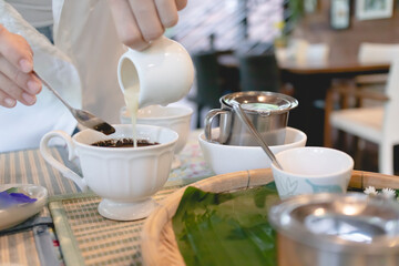 Woman in white shirt is pouring milk into a hot cup of coffee.