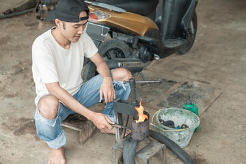 Tire repairman keeps the flame on the traditional press when patching a motorbike tire in a tire repair shop