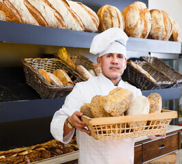bakery male worker with tasty and fresh bread products on counter in the shop