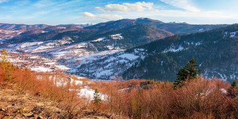 mountainous countryside on a sunny day. late winter scenery or beginning of spring. melting snow and leafless trees on the hills. village in the distant valley. transcarpathia, ukraine