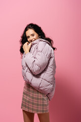  brunette young woman in puffer jacket posing on pink background