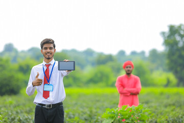 Young indian agronomist showing smart phone with farmer at green chilly field