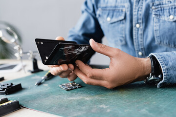 Close up view of disassembled parts of broken smartphone in hands of repairman at workplace on...