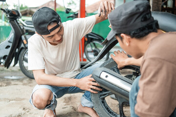 squatting male customer holding a tire while a squatting tire repairman checks a motorbike tire for a leak in a tire repair shop