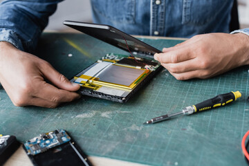 Close up view of repairman hands disassembling broken digital tablet near screwdriver at workplace
