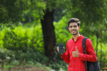 Young indian college student showing smart phone over nature background