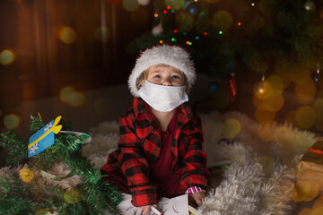 a child in red clothes and medical mask is sitting waiting for the new year. the concept of celebrating Christmas at midnight. holiday costume. a girl writes a letter to Santa Claus. wish list