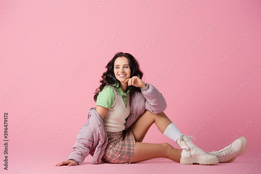 Wall mural  brunette young woman in stylish winter outfit posing on floor on pink background