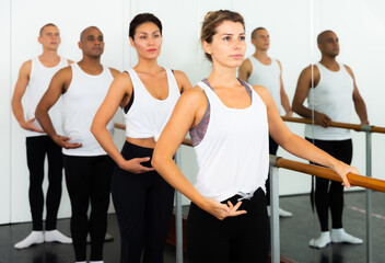 Fototapeta na wymiar Group of people doing ballet exercises using barre in gym with focus to fit athletic toned woman in foreground in health and fitness concept