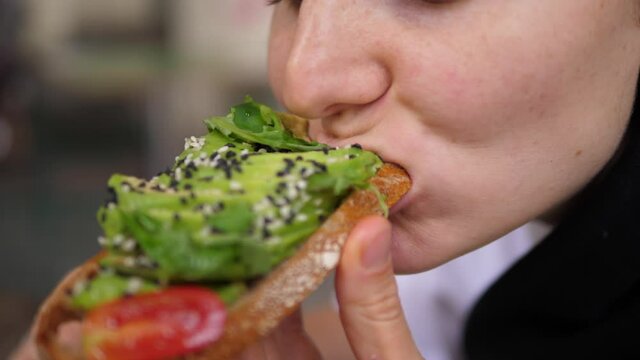Diverse Mediterranean cuisine for health benefits. Vegan woman bites veggie rich toast with avocado slices and leafy greens