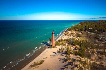 Beautiful aerial photograph of the Little Sable Point Lighthouse situated in Silver Lake Sand Dunes along the blue water shore of Lake Michigan with blue sky above on a sunny autumn day.