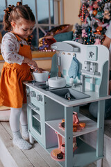 Toy kitchen presents for girls. Christmas present under the tree. Little girl playing toy wooden kitchen and dishes on Christmas. Eco-friendly wooden toys for girls.