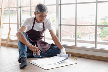 Senior asian old man carpenter check blueprint plan for building diy furniture in workshop