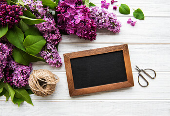 Fresh lilac flowers frame over wooden background with copy space on blackboard, flat lay floral composition