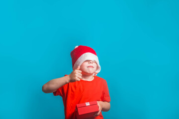 A child in a Christmas Santa Claus costume shows a like on a blue background in the Studio.