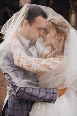 stylish happy bride and groom embracing and hugging under veil, sensual romantic moment.