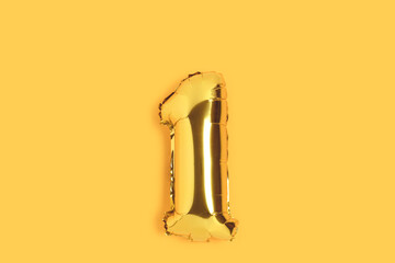 Number 1 golden balloon with copy space. One year anniversary celebration concept on a yellow...