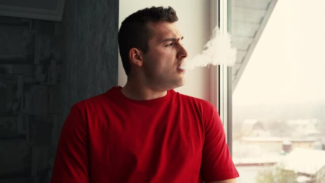 man smoking vape sitting by the window