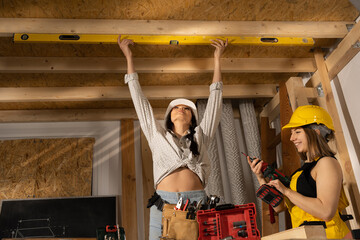 The engineer checks that the beams of the mezzanine floor are exactly horizontal. Blonde and dark haired girls at the construction site.