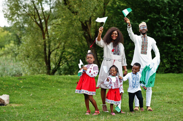 African family in traditional clothes with nigerian flags at park.