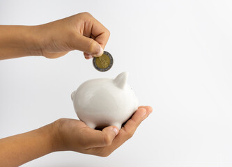 A piggy bank in hand and is putting coins in a piggy bank with copy space on white background.