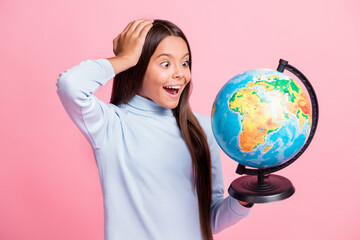 Close-up portrait of lovely cheerful amazed girl holding in hands globe learning countries lesson isolated over pink pastel color background
