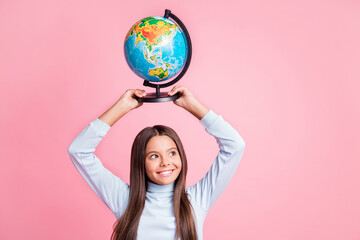 Portrait of attractive cheerful cute girl carrying globe on head learning world map copy space isolated over pink pastel color background