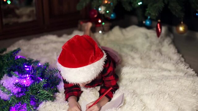 a child in red clothes is sitting waiting for the new year. the concept of celebrating Christmas at midnight. holiday costume. a girl writes a letter to Santa Claus. wish list