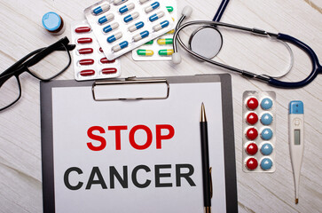 On a light wooden background there is paper with the inscription STOP CANCER, a stethoscope,...