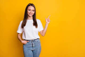 Photo portrait of woman pointing finger at blank space one hand in pocket isolated on vivid yellow colored background
